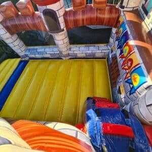 Hüpfburg mit Burgmauern in bunten Farben, ideal für Kindergeburtstag und Events, mit rutschigem gelben Boden und terrakottafarbenen Zinnen, sorgt für Spaß und Abenteuer.